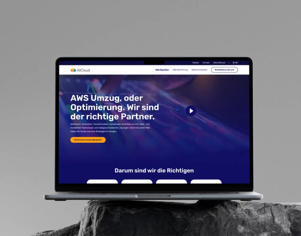 A laptop displaying the allCloud website re-design, featuring text in German about AWS migration and optimization services. The website has a blue and purple theme, with a prominent call-to-action button labeled "Kostenloses Analysegespräch."