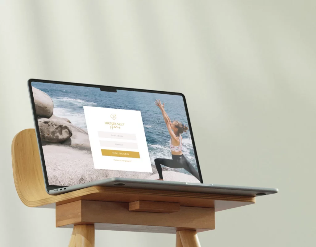 A laptop displaying the Higher Self Home website design by Laura Seiler sits on a wooden stand. The screen shows a login page with a scenic ocean background, featuring a person practicing yoga. This image highlights user experience and UX/UI elements of the website.